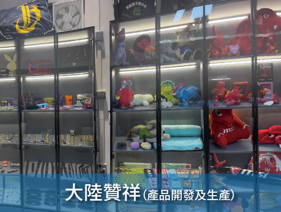 A display cabinet filled with plush toys, figurines, and branded merchandise such as hats and keychains. The blue banner at the bottom reads"Dongguan Zanxiang (Product Development & Manufacturing).